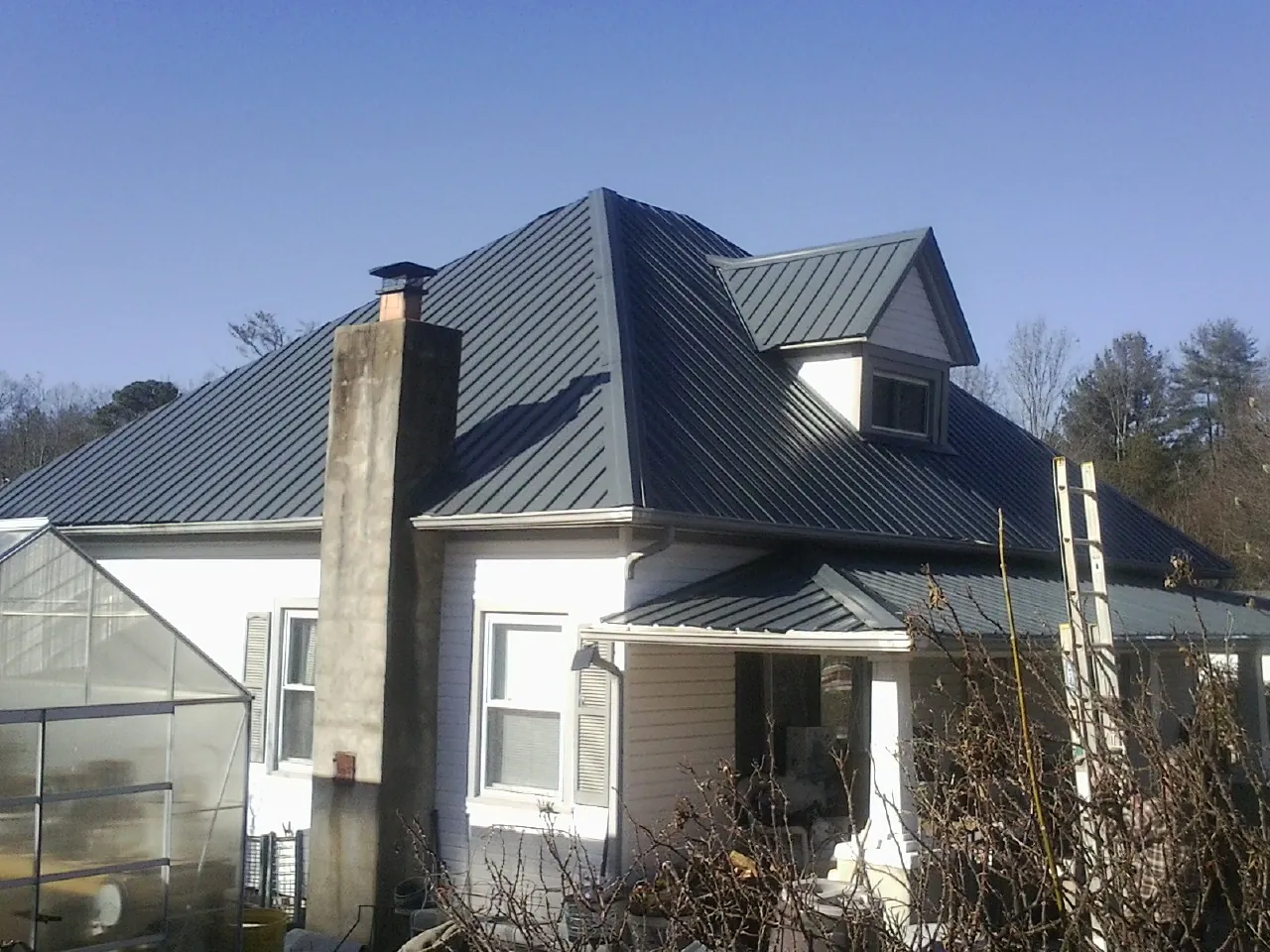 Dark blue standing seam metal roof on a white farmhouse with dormer — Slate & Tile Roof Repair by Roofing Brothers in Thomas