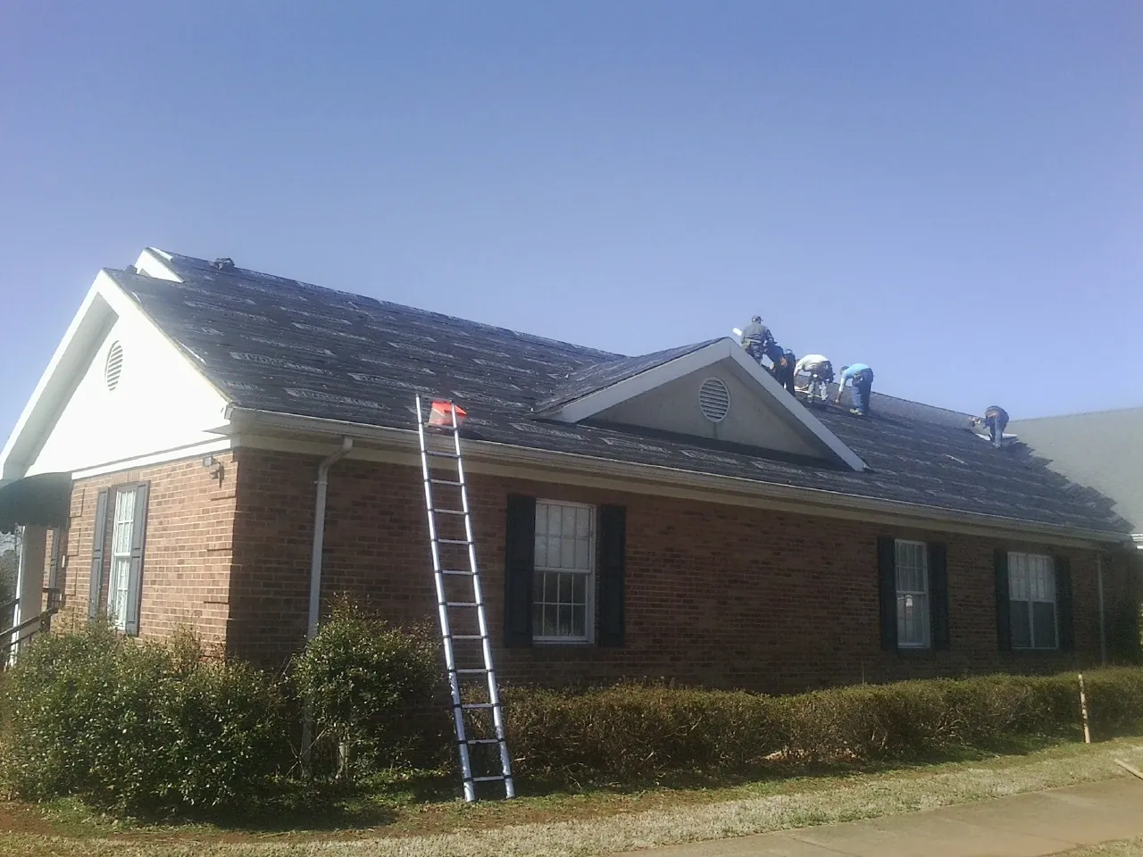 Crew tearing shingles off a brick ranch roof with a ladder set — Emergency Roof Repair work by our crew in Thomas