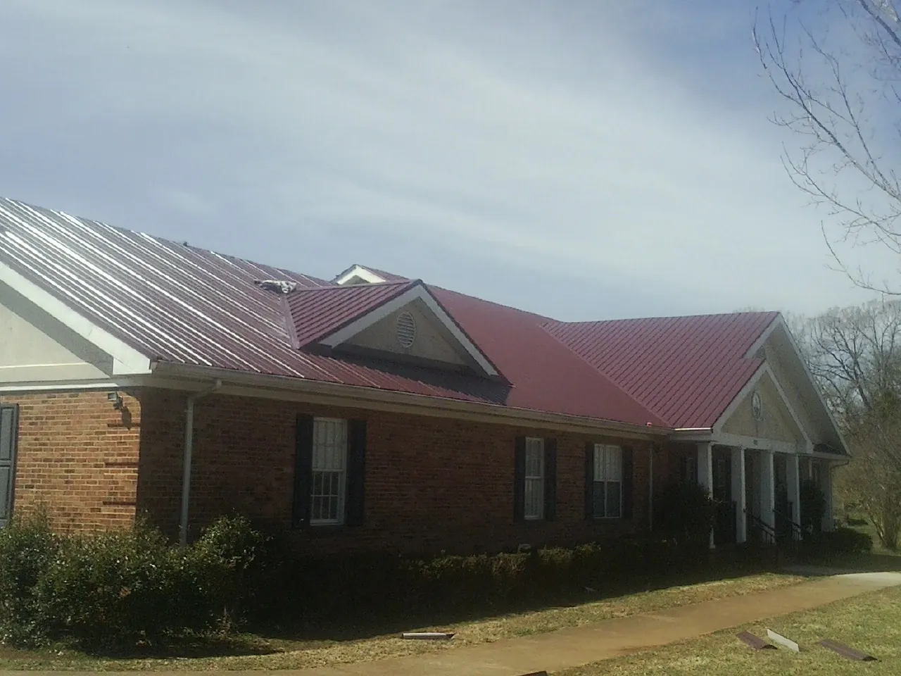 Red metal roof with gabled entries on a long brick building, from a Hail Damage Roof Repair job in Thomas