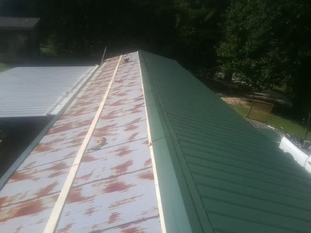 Old rusted panels beside newly installed green metal roofing — Wind Damage Roof Repair by Roofing Brothers in Thomas