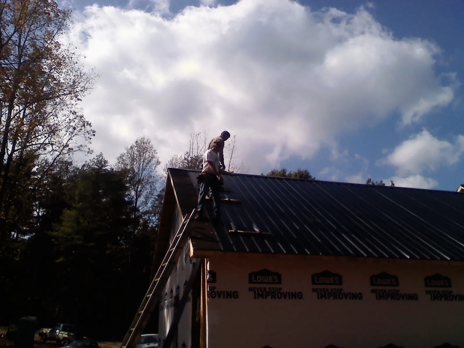 Roofer fastening dark metal panels high against a cloudy sky, from a Roof Inspection job in Thomas
