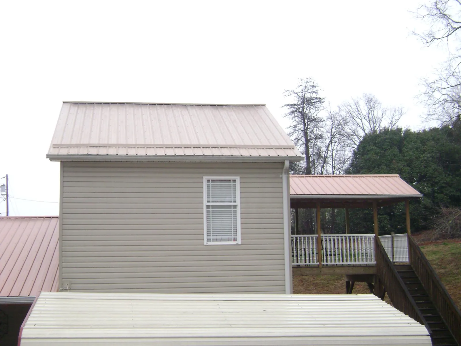 Tan metal roofs on a two story addition and attached porch, from a Roof Replacement job in Thomas